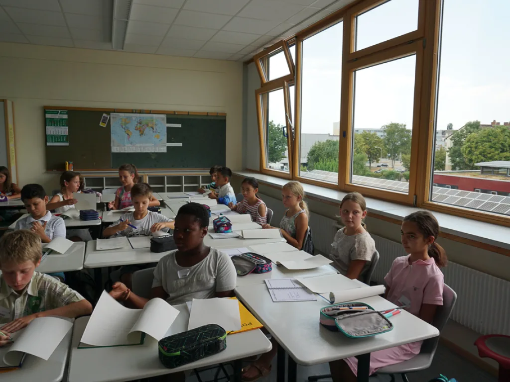 Kinder sitzen an Tischen vor der Fensterfront.